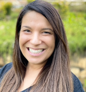 Pictured here is a portrait photograph of Veronica House who is smiling and wearing a black shirt. You can see a green blurry background behind her.