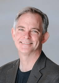 Pictured here is Solon Simmons. He smiles directly at the camera, has a gray background, and wears a gray blazer.