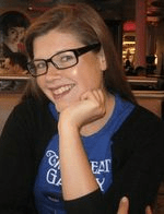 Pictured here is Robyn Russo, shown from the chest up. She wears a blue shirt and a black sweater. She has black glasses and has brown hair. 